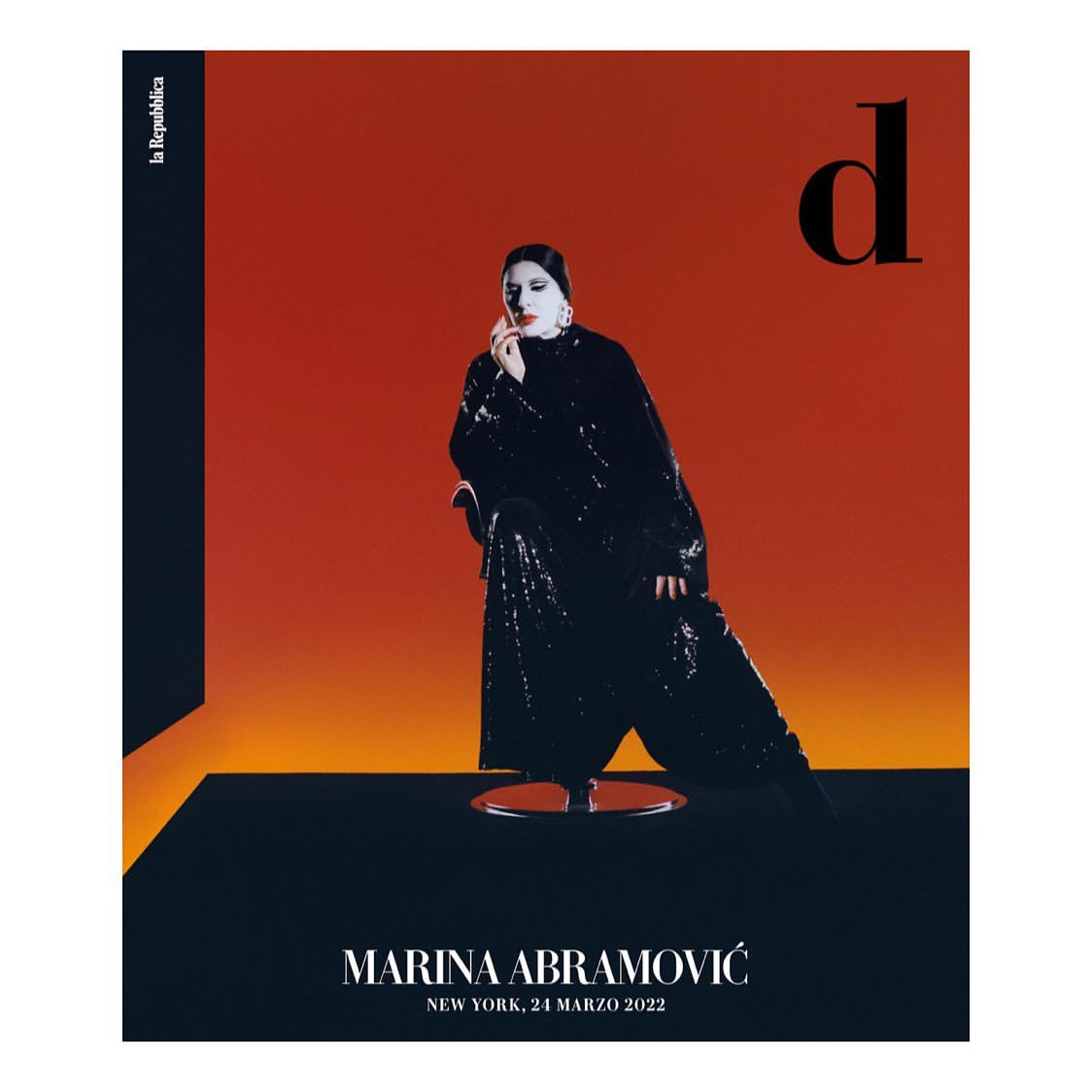 Marina Abramović magazine cover in black sequin outfit against an orange and black backdrop. Portrait with studio lighting.