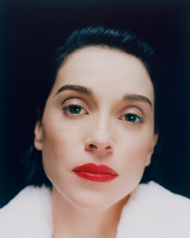 Close-up portrait of an adult woman with fair skin, red lipstick, and dark hair against a dark background, wearing a white fur coat.