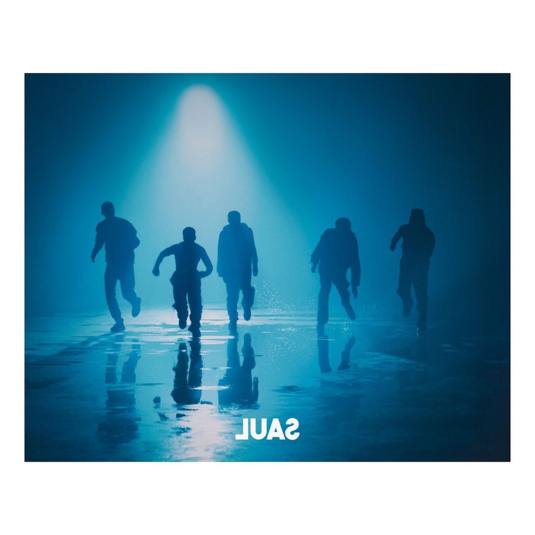Five figures silhouetted and running against a blue spotlight background with reflections on the wet surface below.