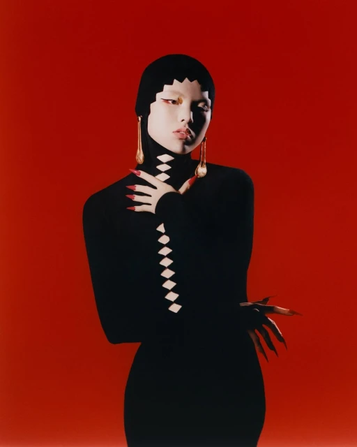 Woman in black turtle neck dress with long red nails poses against red background in portrait fashion shot with unique style.