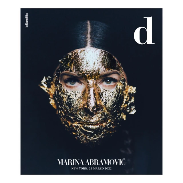 Magazine cover featuring an adult woman with golden foil on her face, a black background, and white text for the publication title.