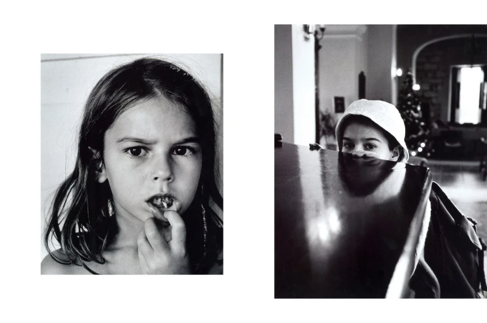 Black and white portrait of a child's face with a missing tooth, plus another child partially visible behind a table indoors.