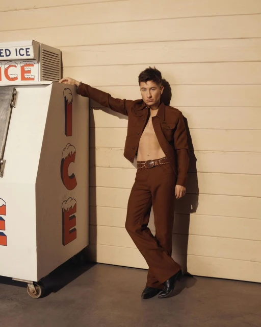 Portrait of a young adult man in a brown suit leaning against an ice machine with an open shirt, complemented by brown and neutral tones.