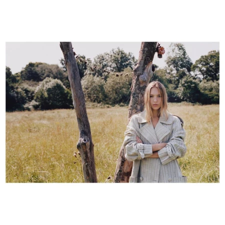 Model standing outdoors in a field wearing a light-coloured coat, styled by Venetia Scott.