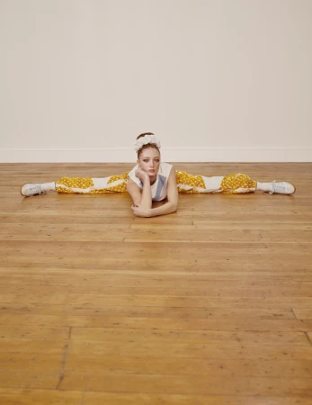 Model doing a split on a polished wood floor wearing patterned trousers and a white top styled by Venetia Scott