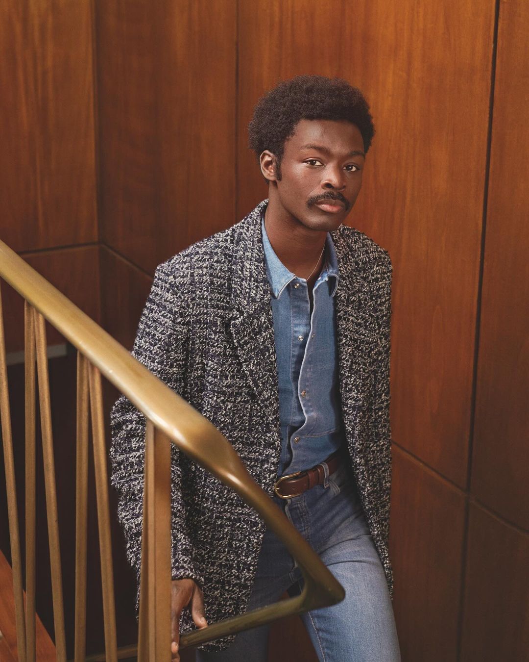 Black man in tweed blazer and denim shirt on staircase styled by Venetia Scott