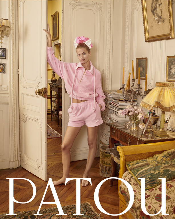 A woman in a pink sweatsuit poses in a doorway of a stylish apartment filled with vintage furniture and framed art in a fashion editorial.