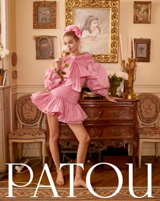 Fashion shot of a fair-skinned adult female posing in a pink dress in an indoor environment with paintings and antique furniture.