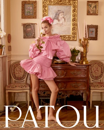 Fashion shot of a fair-skinned adult female posing in a pink dress in an indoor environment with paintings and antique furniture.