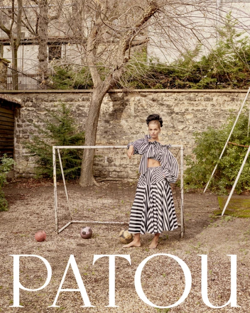 Fashion editorial shot of a slender female model in a striped skirt and top posing next to a soccer goal in an outdoor setting.