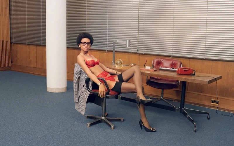 Woman in red lingerie seated on an office chair with a blazer, in a vintage-style office with an old-fashioned desk and carpet.
