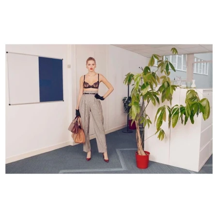 A woman strikes a pose in an office setting, showcasing a stylish ensemble with trousers, gloves, and a bra, holding multiple bags.