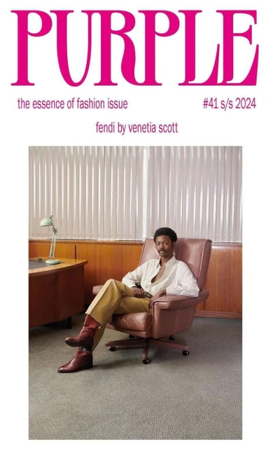 Purple Magazine cover featuring a man seated in an office-style setting wearing a button-down shirt, trousers, and boots.