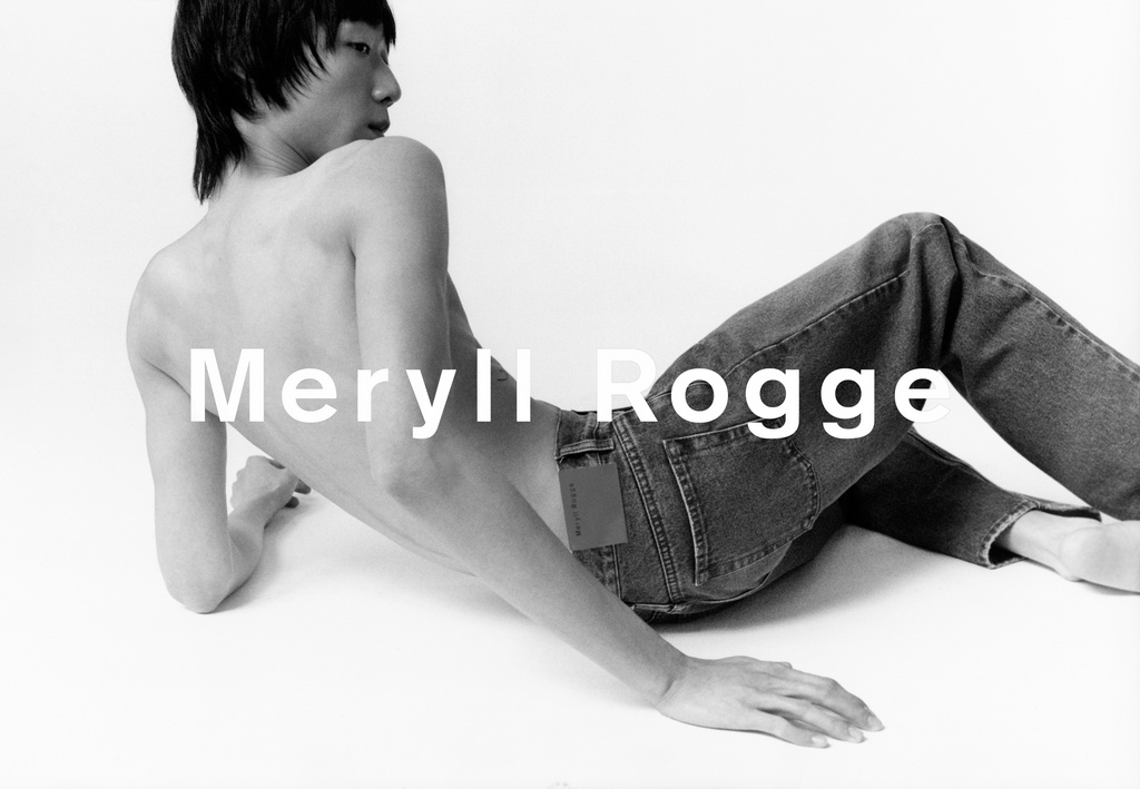 Asian male model poses in jeans on a white background for a studio fashion shot. The model is shirtless and looking over his shoulder.