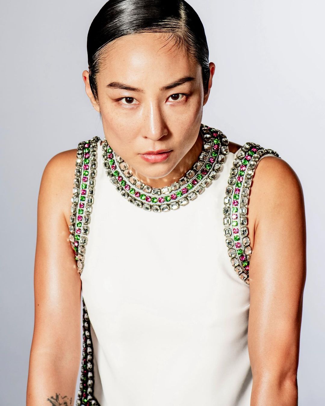 Close-up studio portrait of an Asian adult female with sleek dark hair wearing a white dress with jeweled neckline, gazing directly at the camera.