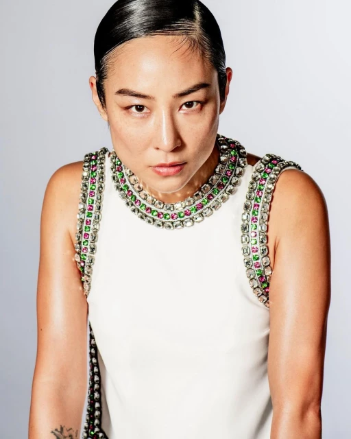 Close-up studio portrait of an Asian adult female with sleek dark hair wearing a white dress with jeweled neckline, gazing directly at the camera.