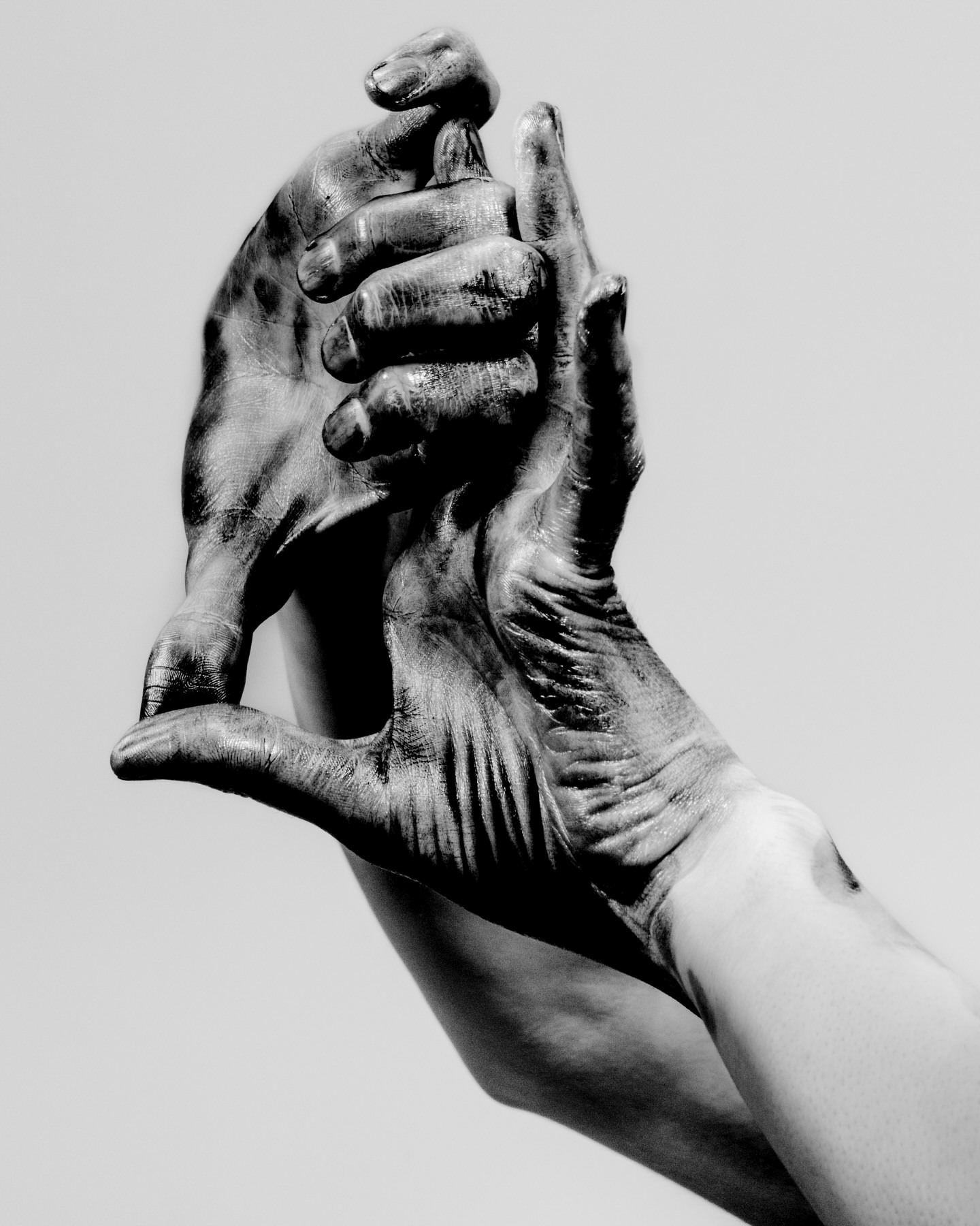 Monochrome image of two hands clasped, fingers intertwined, with a contrasting dark coating against a neutral background.