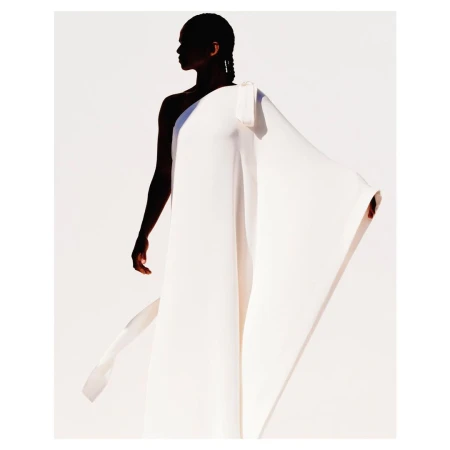 Elegant portrait of a woman wearing a flowing white gown against a white background, captured in soft studio lighting with shadow.