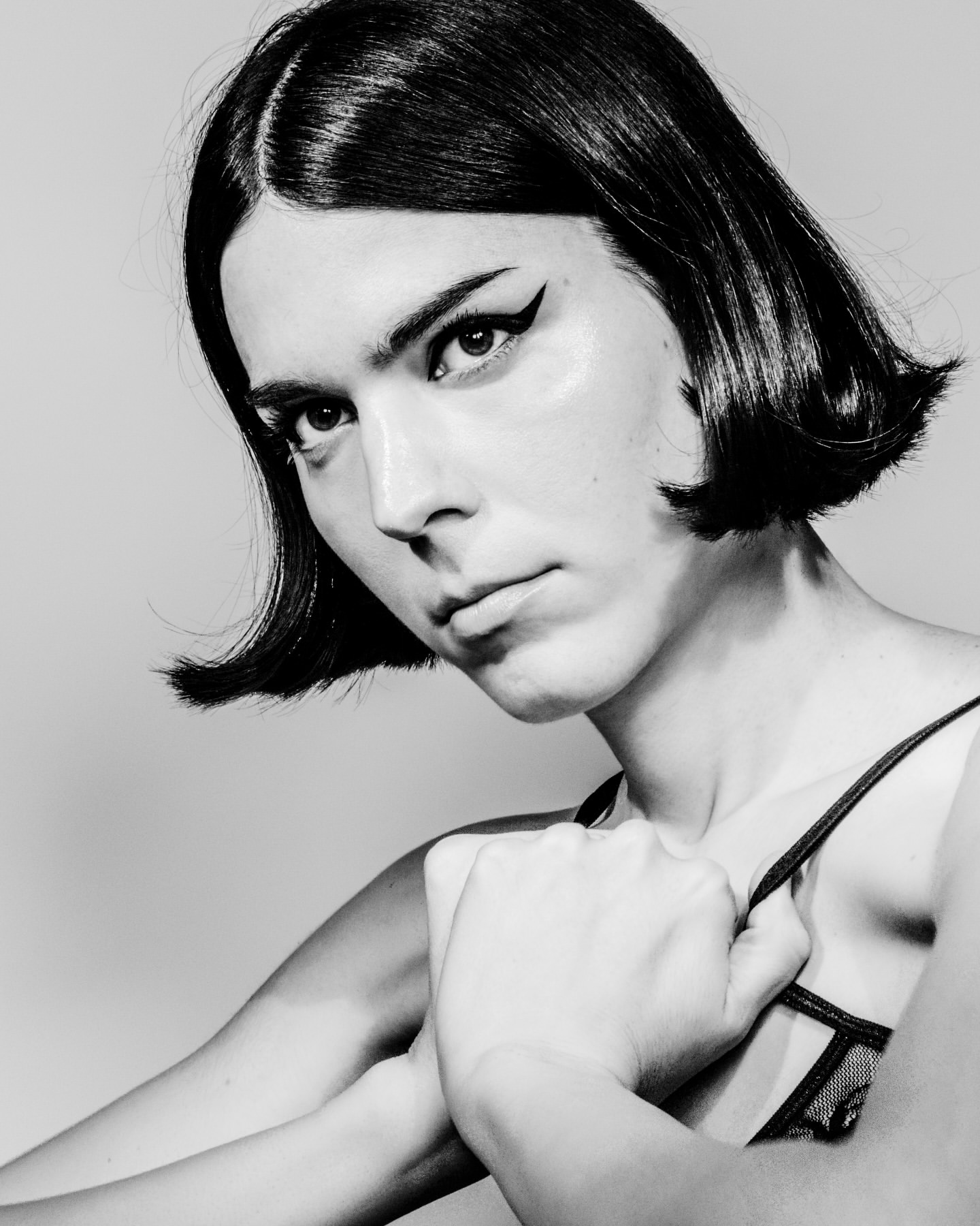 Black and white portrait of a young adult female with short black hair, wearing a lace top, with a neutral facial expression in a studio.