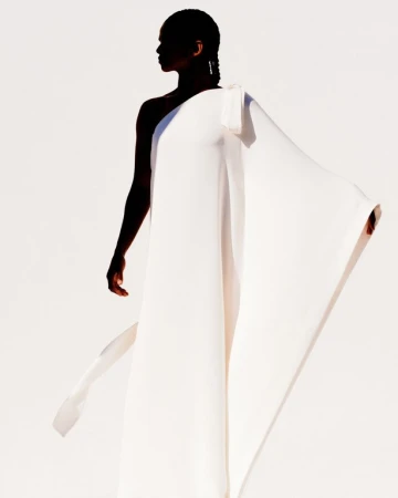 Model in flowing white one-shoulder gown standing against a plain bright white studio background.