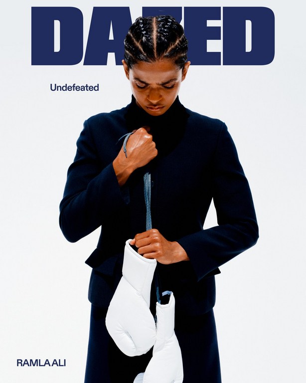 Ramla Ali on Dazed magazine cover wearing a black suit, holding white boxing gloves on a bright white background. 