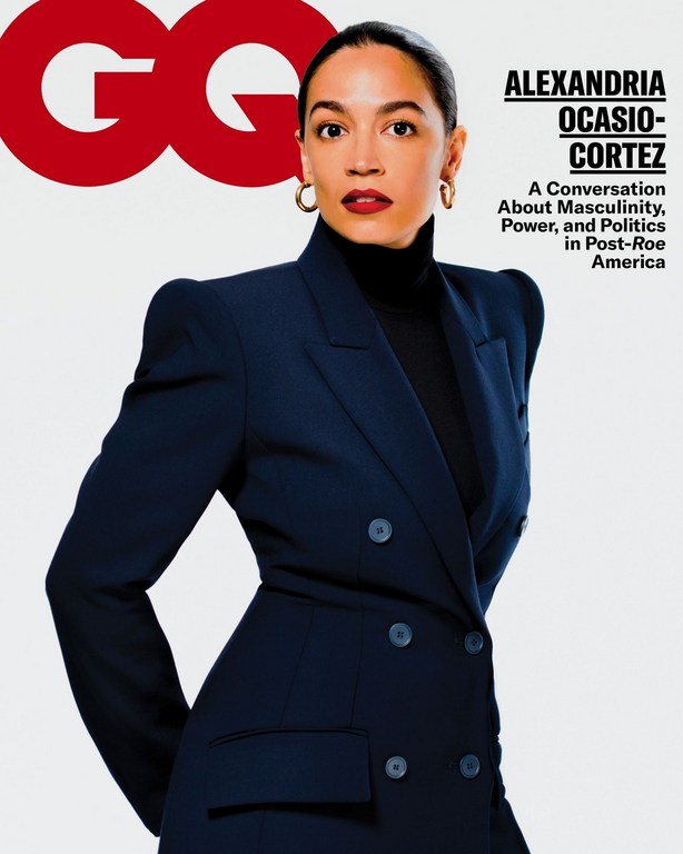 Alexandria Ocasio-Cortez poses on the cover of GQ magazine wearing a dark blue suit against a white background in a studio setting.