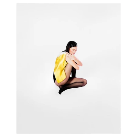Model wearing a yellow top and sheer black tights crouching against a bright white seamless background.