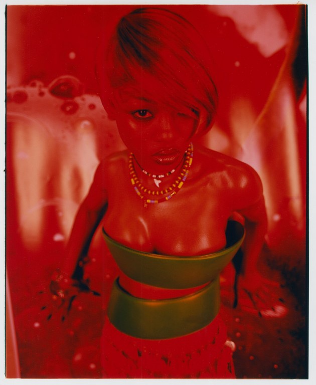 Digitally rendered woman with short blonde hair, wearing a two-piece outfit with beaded necklaces, against a red and orange background.