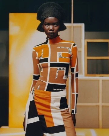 Model in geometric patterned turtleneck top and matching skirt wearing a dark sculptural hat