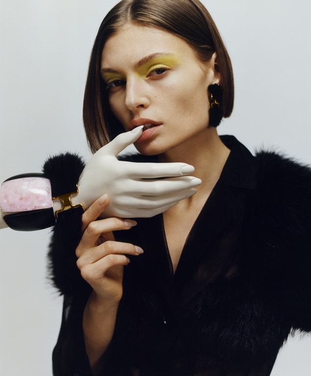 Close-up of a fair-skinned woman with yellow eyeshadow and bob haircut, wearing a black top with a prosthetic hand on her neck.