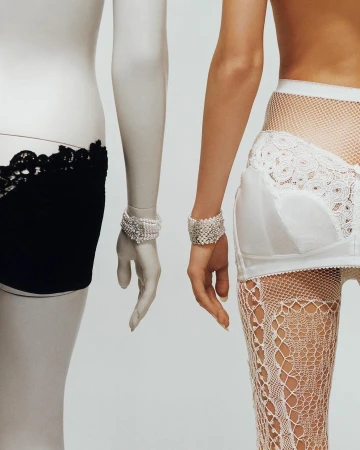 Close-up of two torsos with arms, one mannequin in black briefs, the other a woman with hosiery and white undergarments, jewelry.