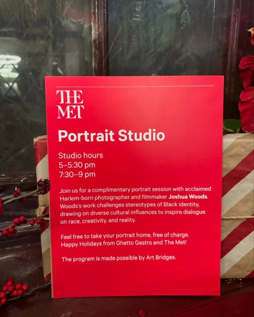 Red promotional sign for a portrait studio at The Met with session hours listed, surrounded by a holiday-themed gift and greenery.