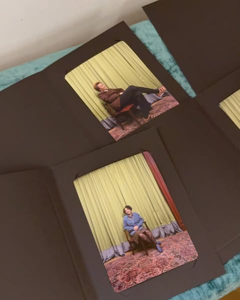 Photographs of an adult man and woman seated in chairs are presented in black paper frames, against a soft blue fabric background.
