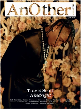 AnOther Magazine cover featuring Travis Scott. Close-up shot of the musician in a black satin-like jacket, flower arrangement background.