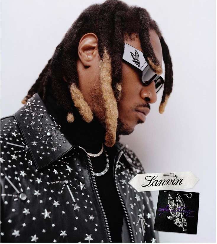 Portrait of a Black man with dreadlocks wearing futuristic sunglasses and a studded leather jacket against a neutral backdrop.