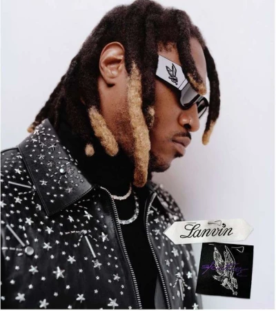 Portrait of a Black man with dreadlocks wearing futuristic sunglasses and a studded leather jacket against a neutral backdrop.