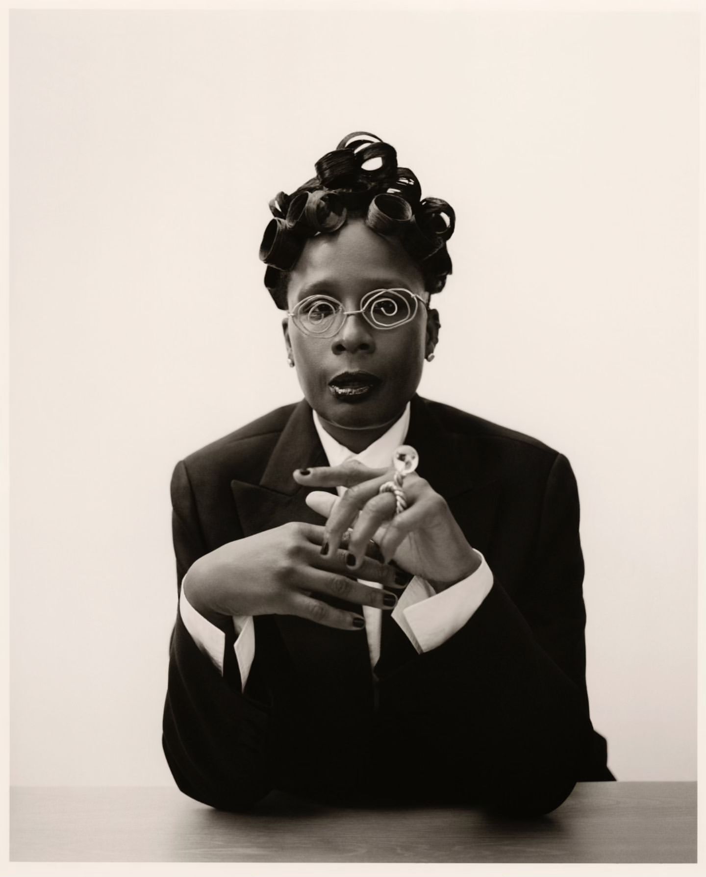 Portrait of a person with sculpted hair wearing a suit and wire glasses by Joshua Woods