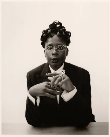 Portrait of a person with sculpted hair wearing a suit and wire glasses by Joshua Woods