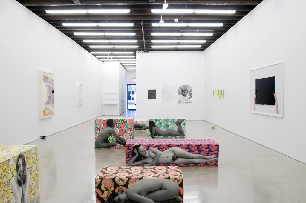 Art gallery exhibition featuring figurative artworks of women printed on rectangular display blocks in a bright, spacious indoor setting.