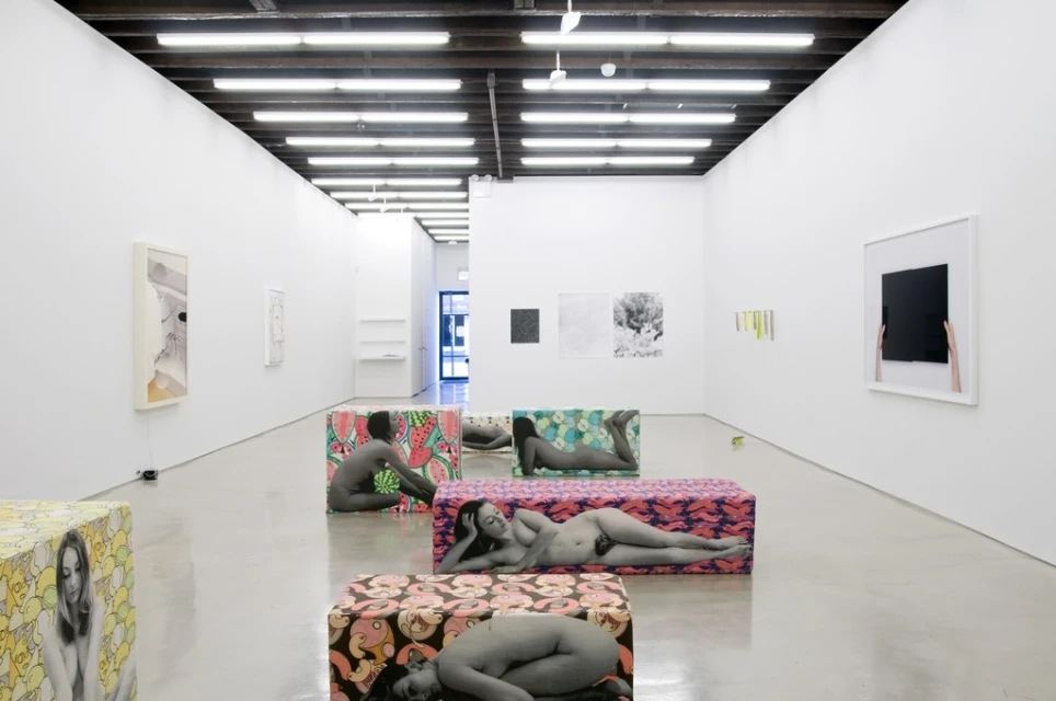 Art gallery exhibition featuring figurative artworks of women printed on rectangular display blocks in a bright, spacious indoor setting.