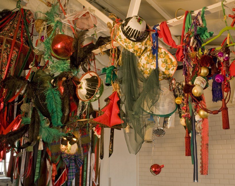 Overhead view of an artistic installation with a variety of ornaments, fabrics, feathers, and decorative items suspended from a white ceiling.