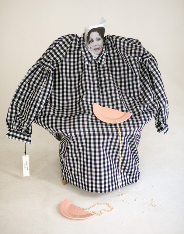 Stylized image with a black and white gingham shirt draped over a form, accessorized with pink plates and a pearl necklace.