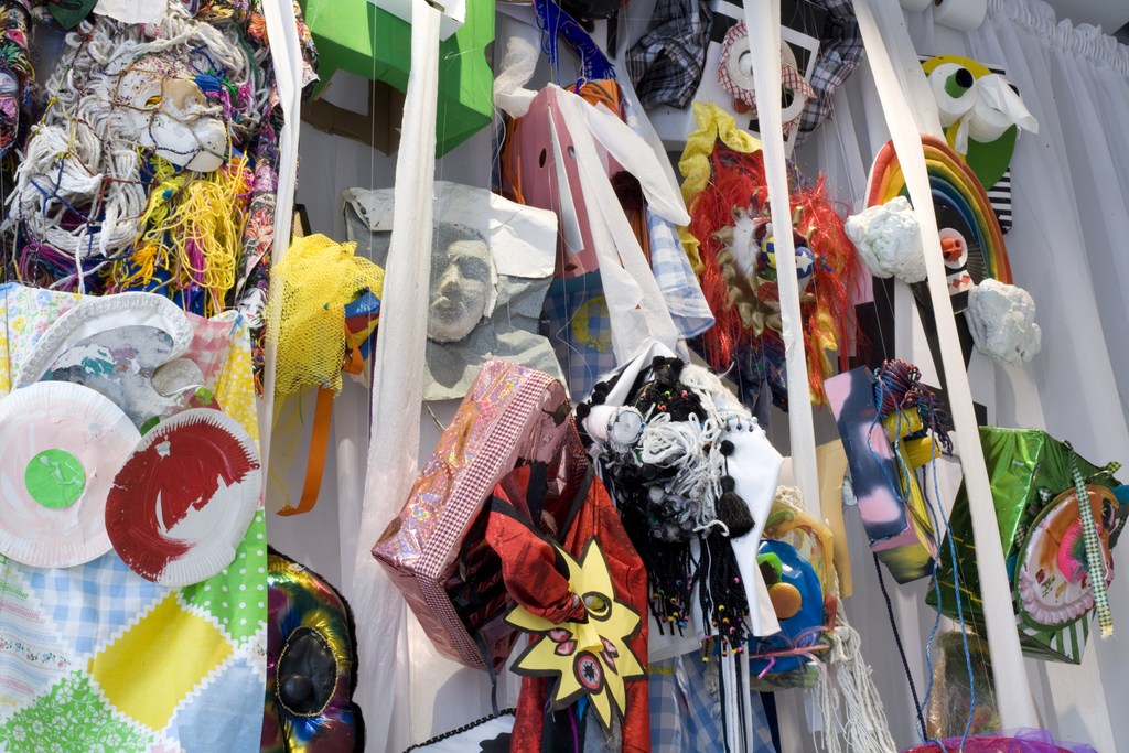 Eye-level shot of a wall-mounted art installation with colorful mixed media elements including cloth, paper, and sculptural forms.