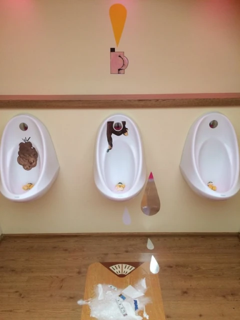 Humorous restroom art featuring urinals with comical characters and illustrations, set against a peach wall and wooden floor.