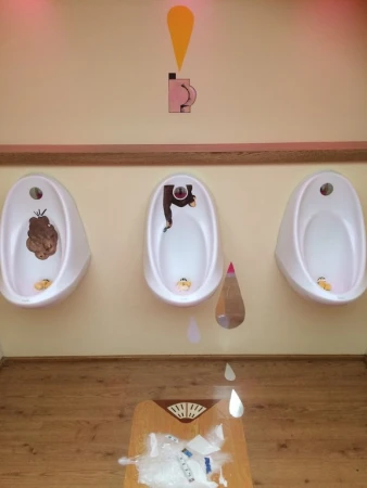 Humorous restroom art featuring urinals with comical characters and illustrations, set against a peach wall and wooden floor.