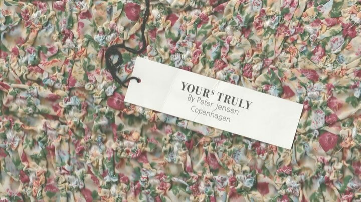 Close-up of a fabric with a floral pattern and a tag that reads YOURS TRULY, By Peter Jensen Copenhagen, showing texture and design.
