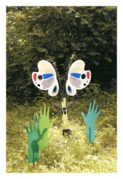 Colorful artistic sculpture featuring butterfly wings and green hand cutouts installed in a dense green outdoor woodland setting.