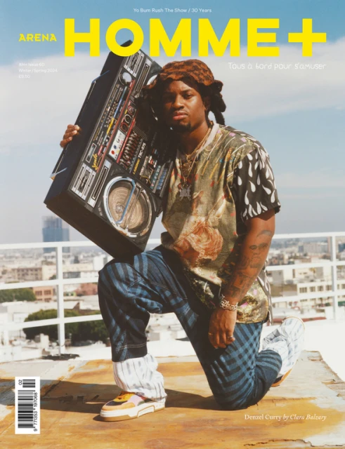 Arena Homme+ magazine cover featuring Denzel Curry holding a boombox on a rooftop with a city skyline in the background. The image has a bright, sunny feel.