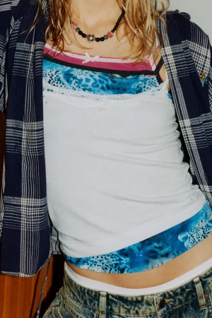Close-up of a model wearing layered tops, beaded necklace, plaid flannel shirt, and denim jeans styled by Helga Burrill.