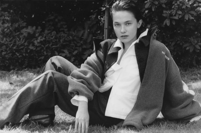 Model seated on grass wearing a wool jacket and trousers styled by Helga Burrill